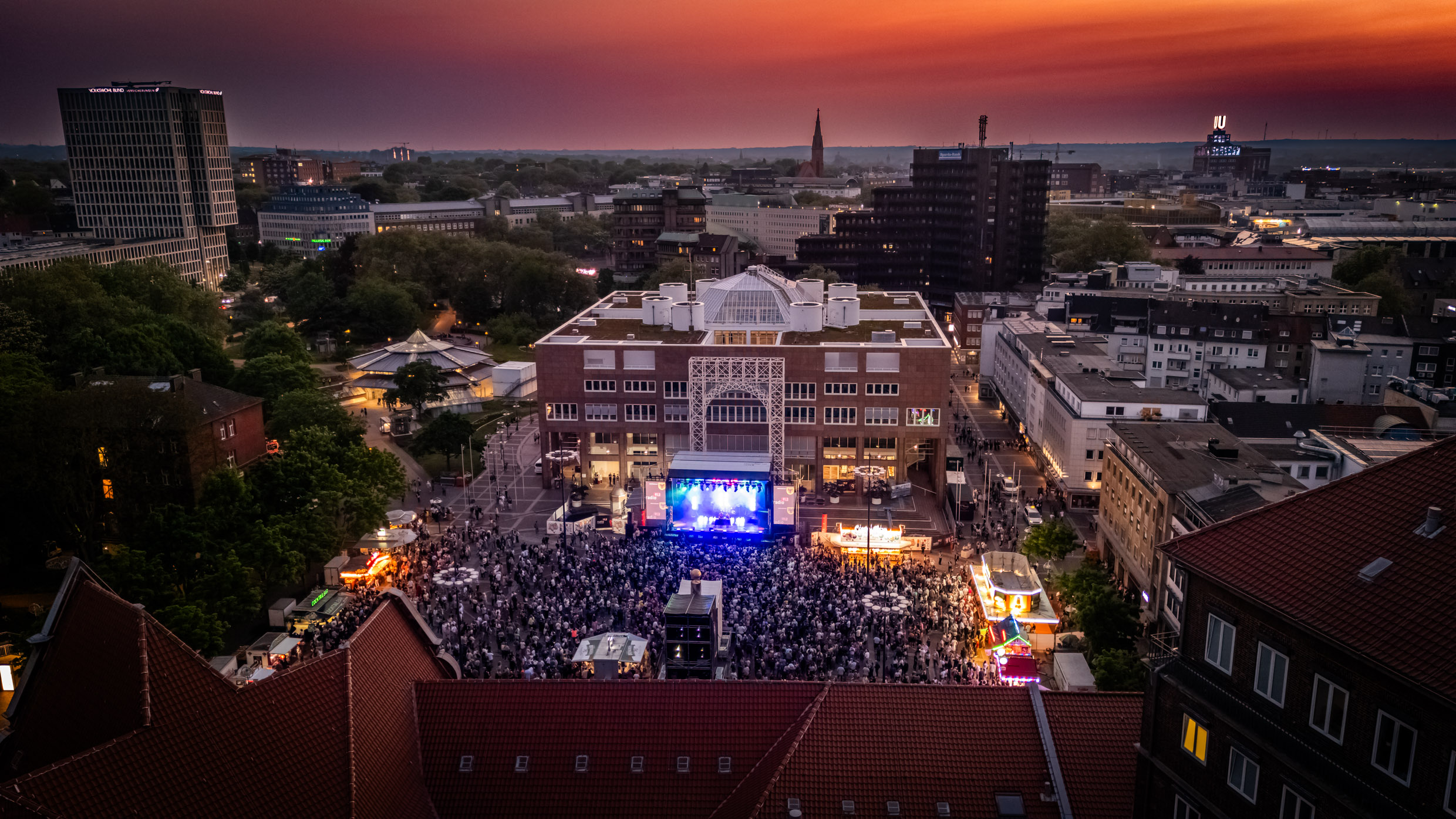 Luftbild vom Friedensplatz Dortmund bei Sonnenuntergang und mit Publikum vor der Dortbunt-Bühne.